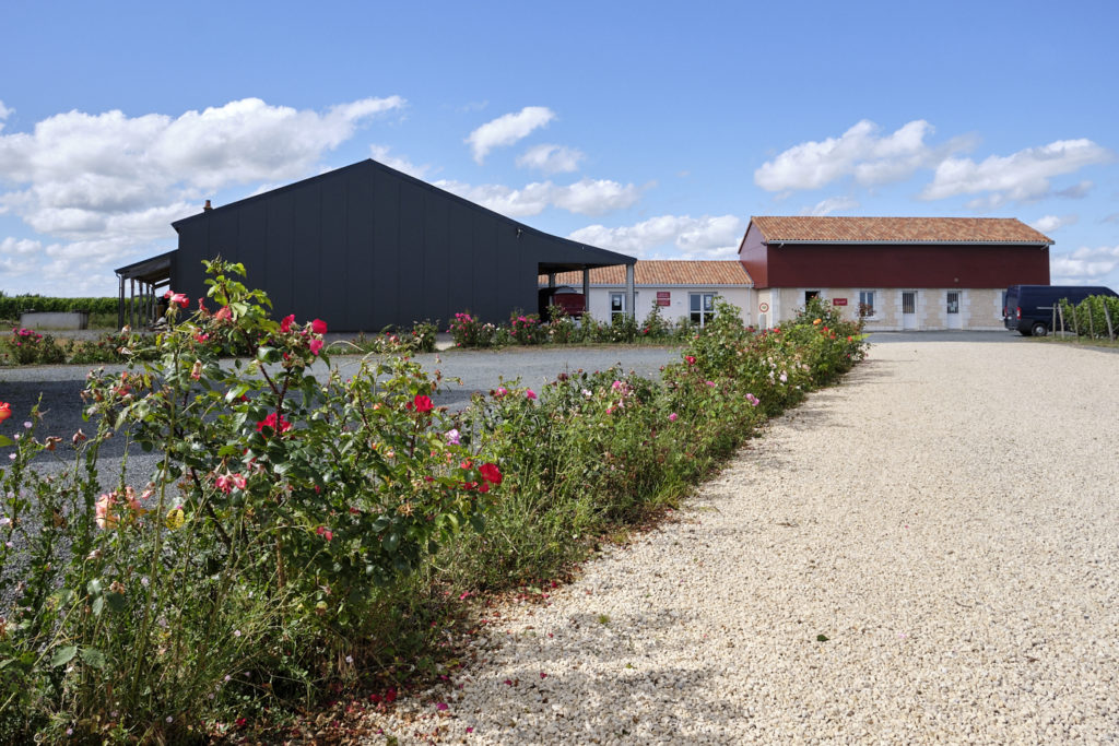 La belle entrée d'un domaine viticole, avec oenotourisme, hangar à matériel et un parterre de fleurs